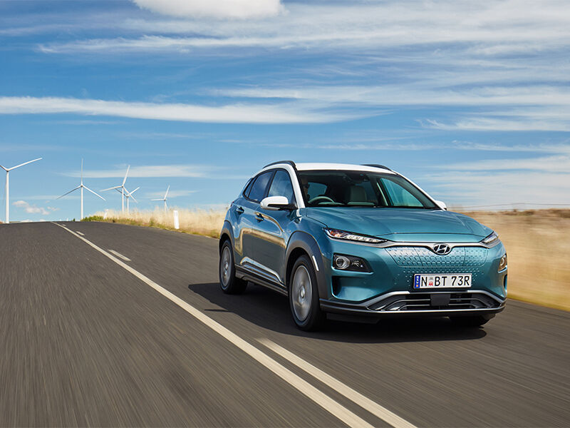Hyundai Kona Electric driving down road with windmills in background
