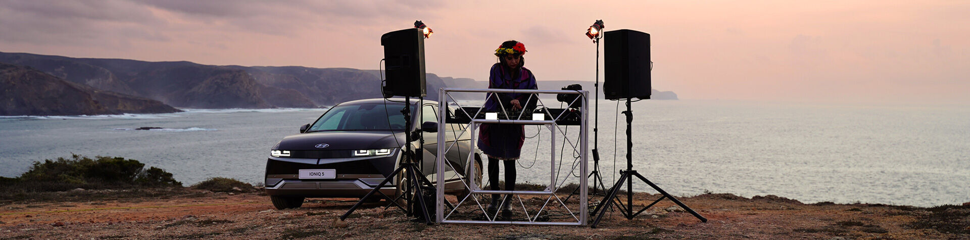 A black IONIQ 5 standing on the edge of a peninsula powering a DJ deck and lighting.