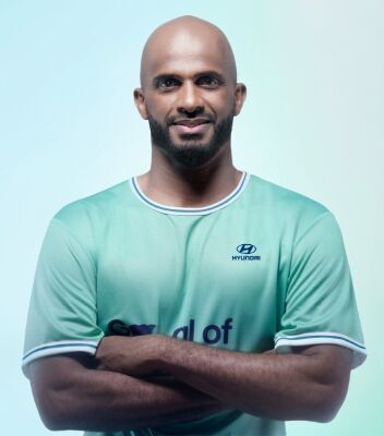 Frontal torso view of new Team Century member Ali Al-Habsi smiling straight into the camera with his arms folded wearing a green Team Century shirt with the blue Hyundai logo and Goal of the Century emblazoned across the front. 