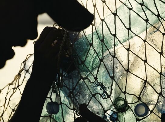 An unseen person holding onto a fishing net filled with plastic bottles.