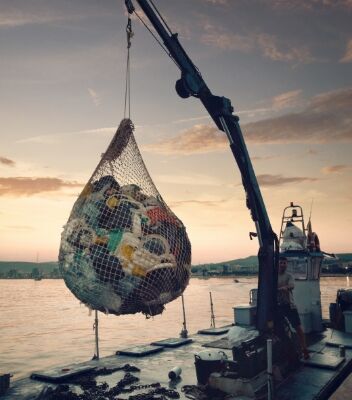 A crane lifting a fishing net full of plastic waste at sunset.
