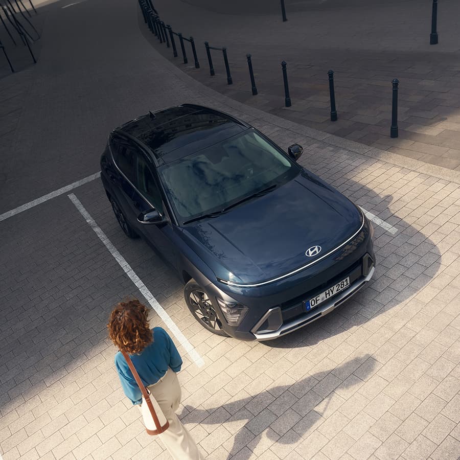 Une femme marchant près de Hyundai KONA Hybrid qui est garé sur une place de parking