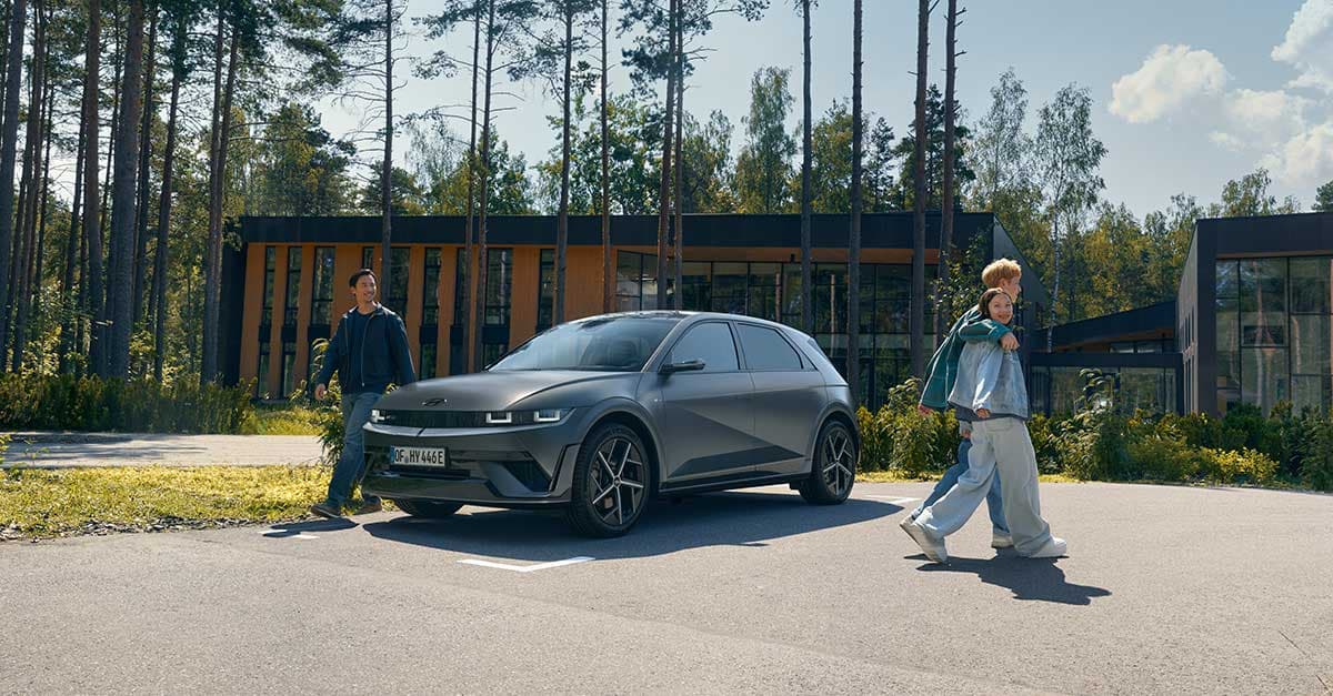 Noen mennesker går rundt en IONIQ 5 parkert foran et moderne hus. Foto.