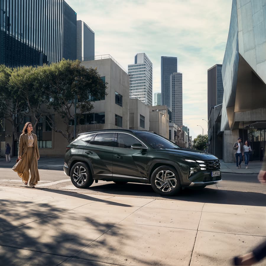 Mörkgrön Hyundai TUCSON parkerad på en stadsgata med höga byggnader i bakgrunden.