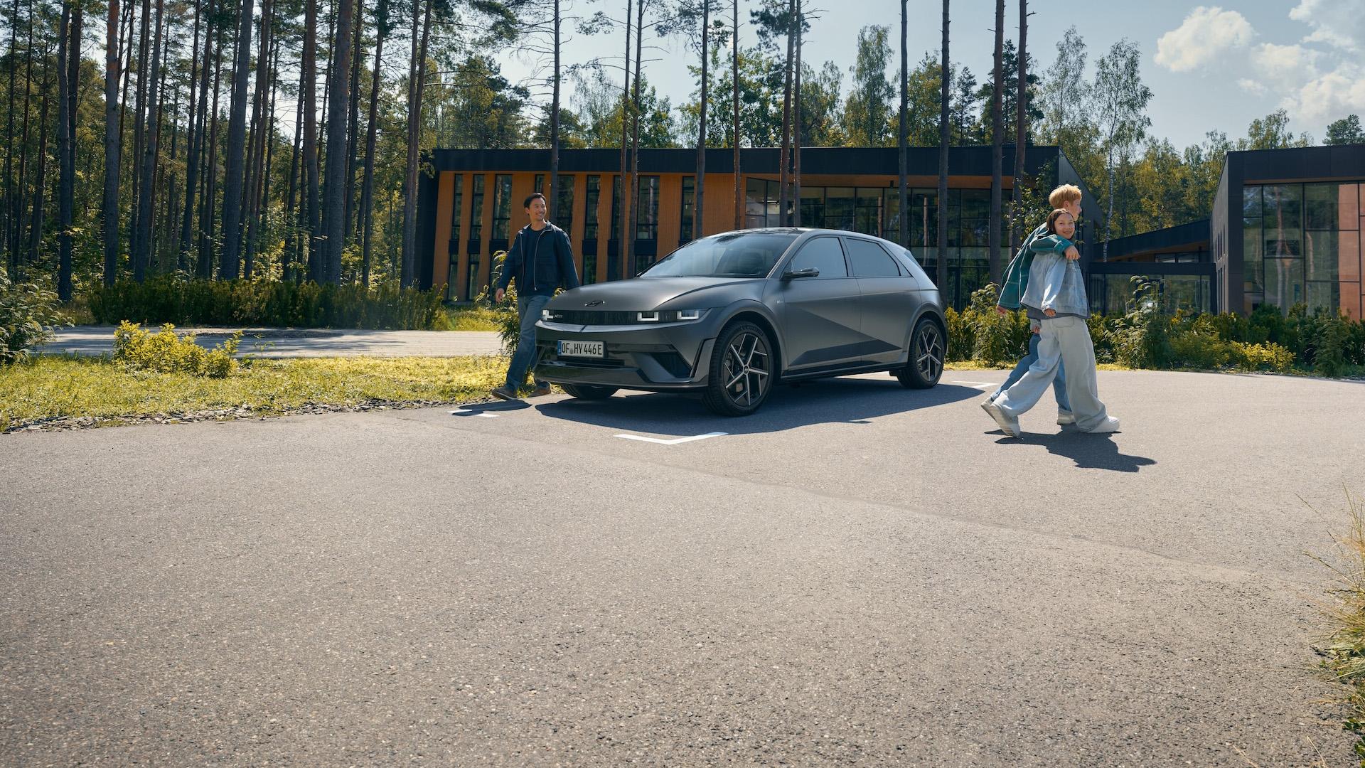 Ein Mann steht neben einem Hyundai IONIQ 5, der auf einem asphaltierten Parkplatz steht, während ein Paar vom Auto weggeht.