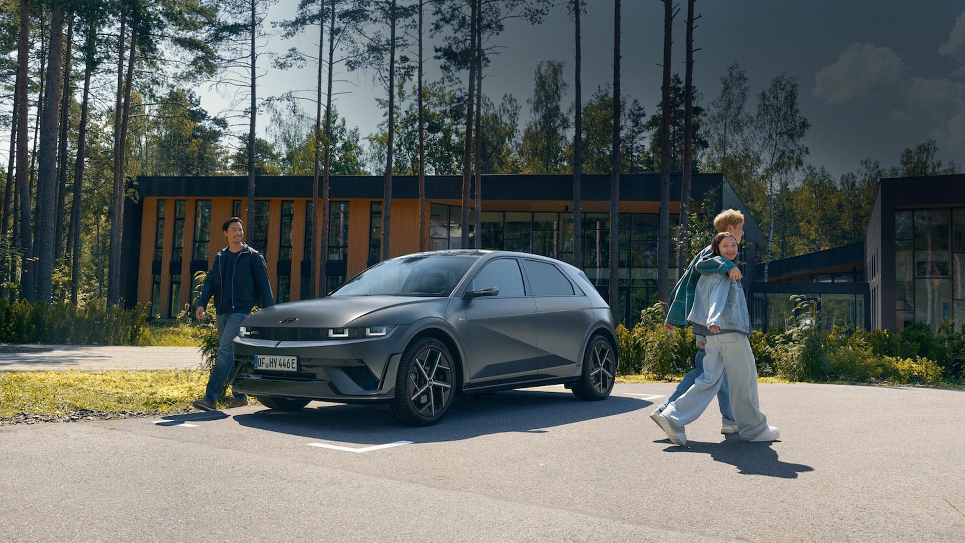 En IONIQ 5 står parkert foran et hus med mennesker som beveger seg rundt bilen. Foto.