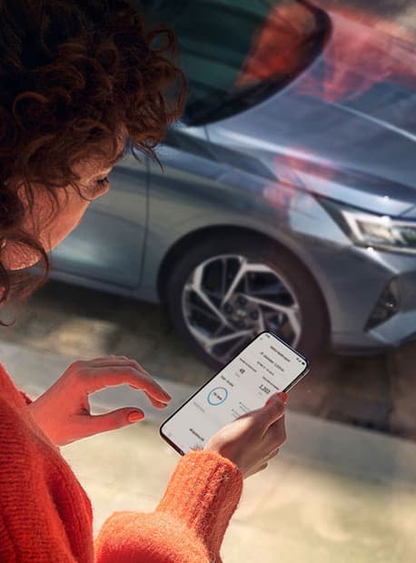 En dame står å sjekker Bluelink-appen på telefonen. Foto.