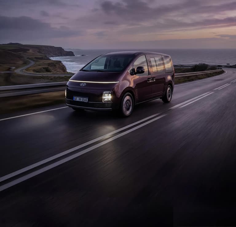 Der Hyundai STARIA Elektro fährt bei Sonnenuntergang entlang einer Küstenstraße.