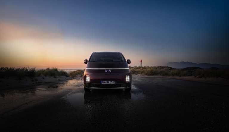 Der Hyundai STARIA Elektro fährt bei Sonnenuntergang entlang einer Küstenstraße.