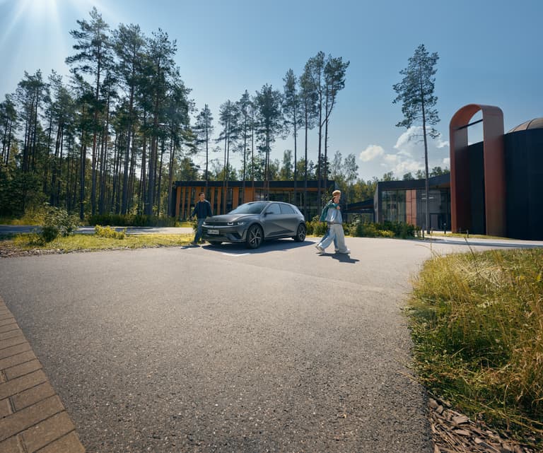 Ein Mann steht neben einem Hyundai IONIQ 5, der auf einem asphaltierten Parkplatz steht, während ein Paar vom Auto weggeht.