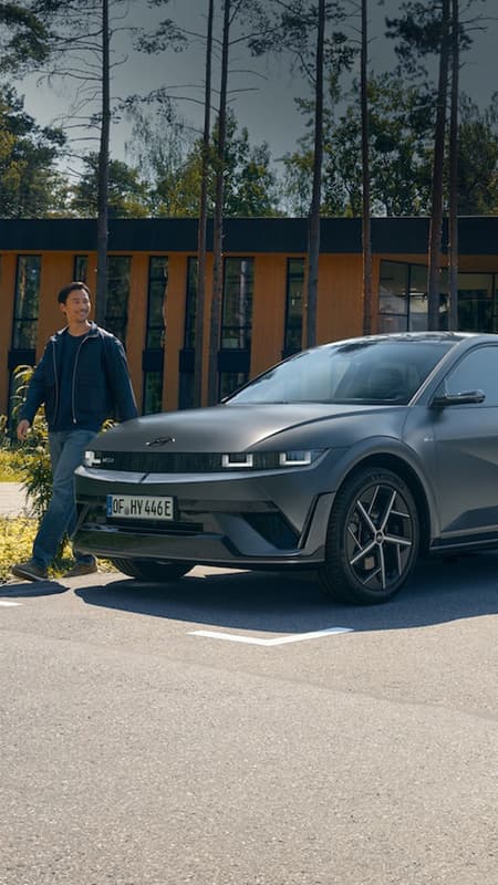 En IONIQ 5 står parkert foran et hus med mennesker som beveger seg rundt bilen. Foto.