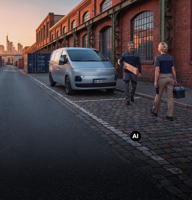 Hyundai STARIA Cargo parkerad utanför en tegelbyggnad, med två personer och arbetsutrustning bredvid bilen.