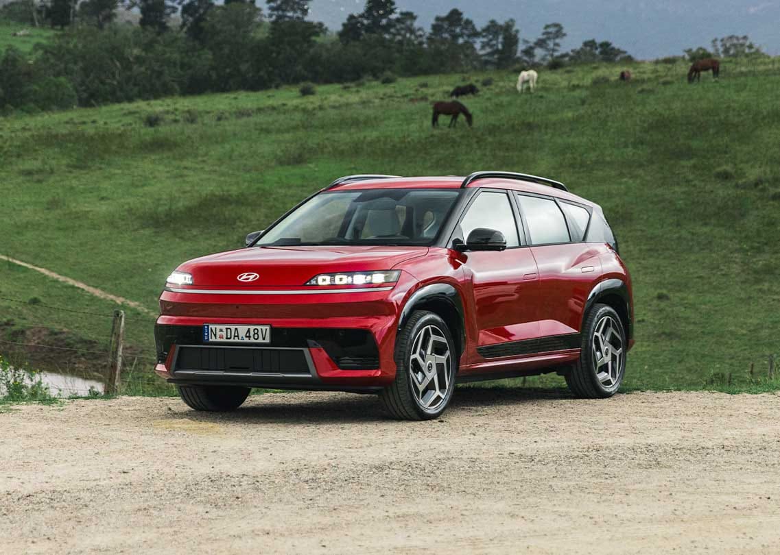 Hyundai ELEXIO electric SUV in red, featuring a modern exterior design and advanced EV styling, photographed in a picturesque countryside setting.