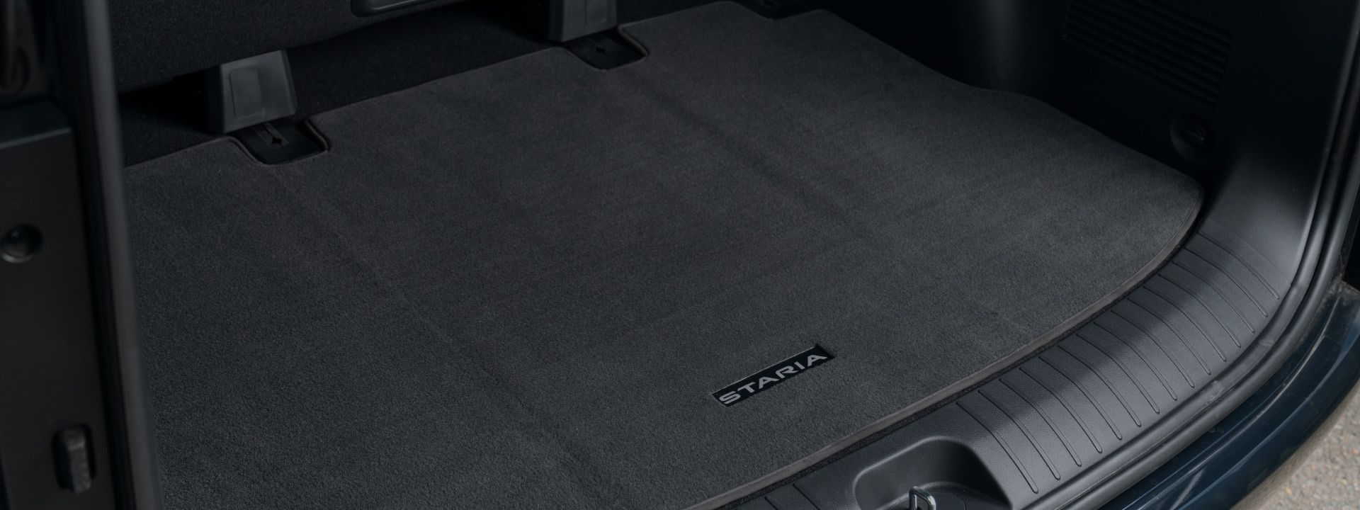 The rear cargo area of a Hyundai STARIA featuring a clean, carpeted floor mat with the “STARIA” logo. 