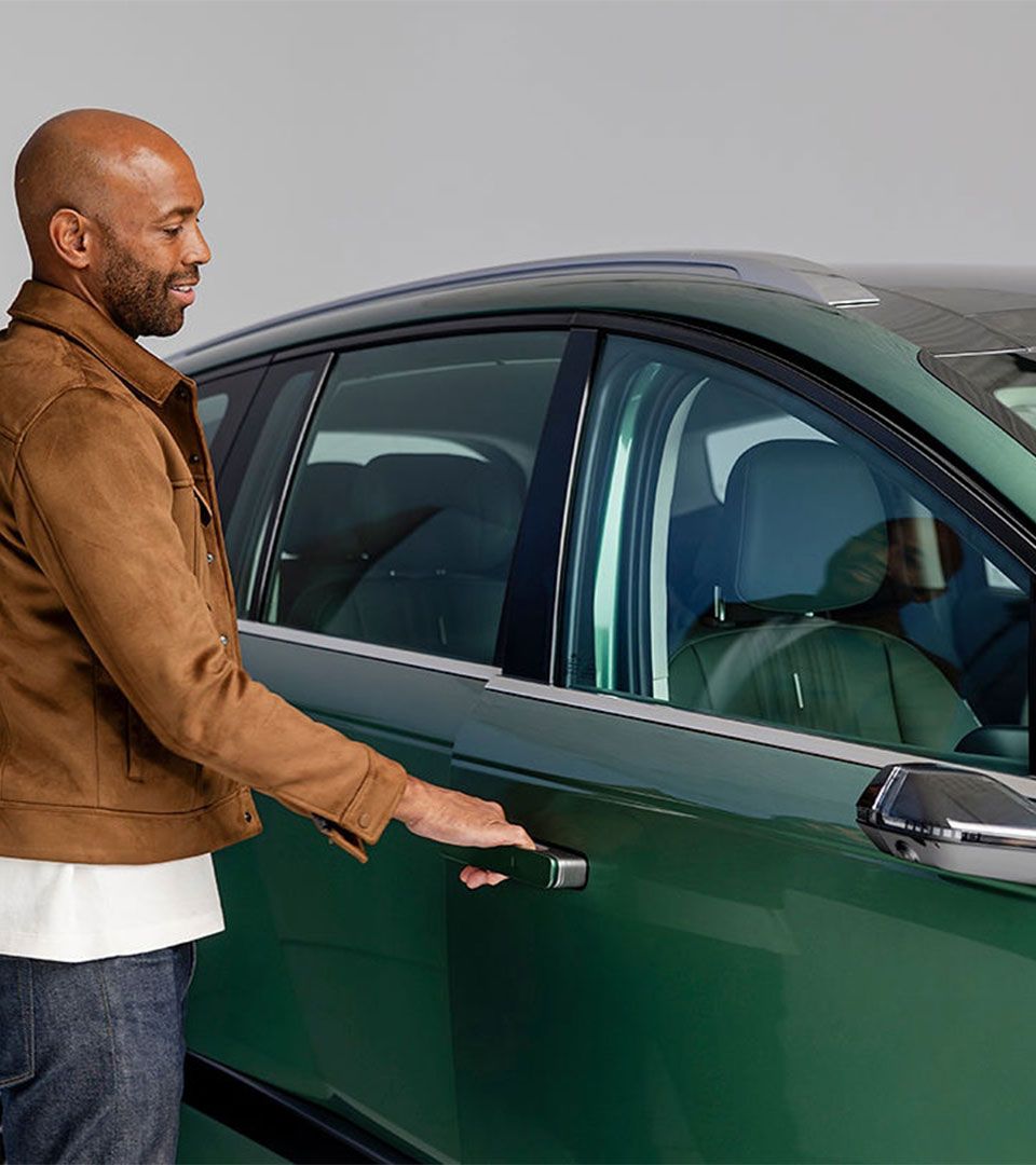 A man wearing a brown jacket uses the keyless entry system to unlock a green Hyundai IONIQ 9, demonstrating the vehicle's smart access technology.