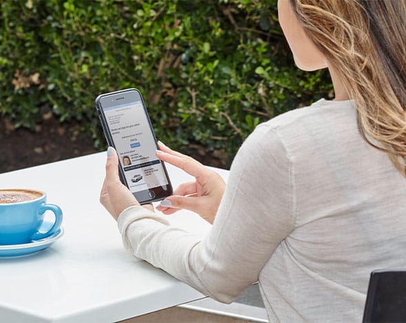 Person using a smartphone at an outdoor café table, viewing a vehicle finance page, representing flexible fleet finance and online application options for Hyundai.