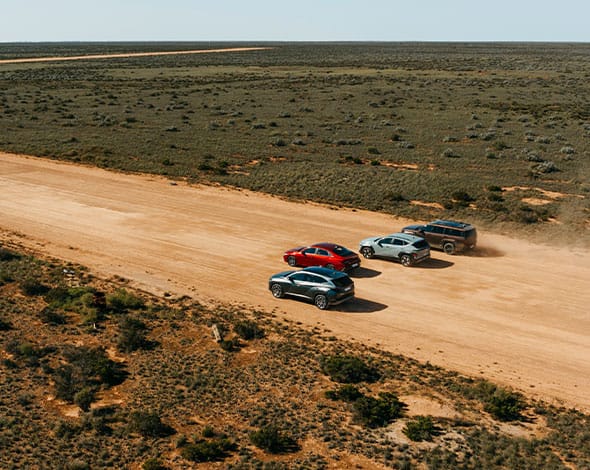 Aerial view of four Hyundai vehicles driving along a dusty outback road through a wide, remote landscape, showcasing fleet capability and versatility across terrain.