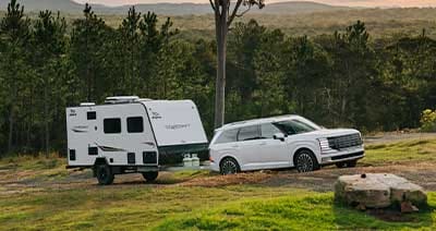 Hyundai PALISADE towing a Jayco Starcraft caravan through a scenic bushland campsite, showcasing strong towing capability, comfort, and versatility for family road trips and outdoor adventures.