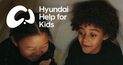 Two children share a joyful moment inside a cozy space, embodying the warmth, care, and community spirit of Hyundai Help for Kids supporting brighter futures through compassion and connection.