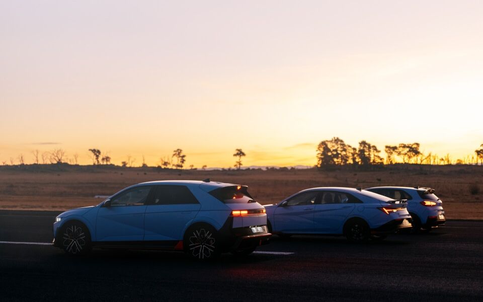 A row of Hyundai N cars stretches along the road, framed by the soft glow of the evening sky.