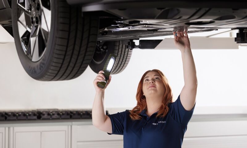 A hyundai technician is carefully examining the car