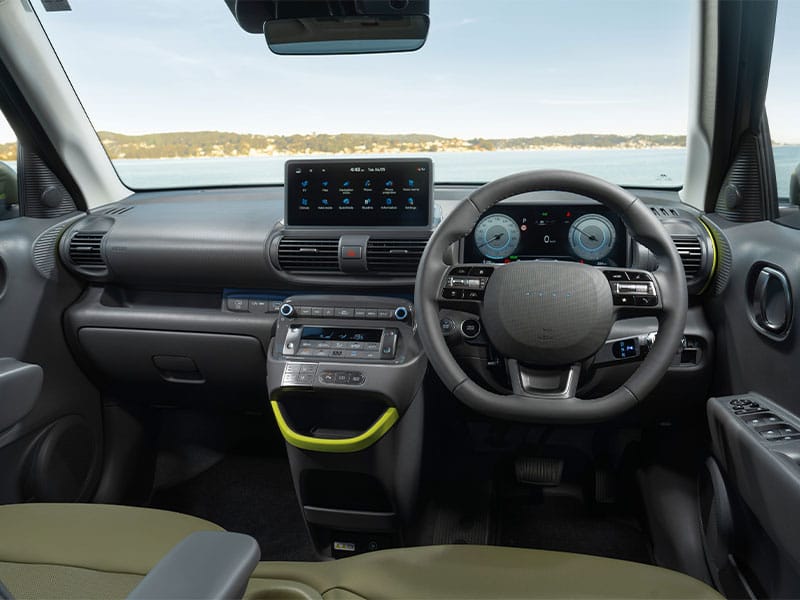 Hyundai Inster cockpit with digital cluster, neon-accented console, and scenic water view ,tech-forward and stylish.