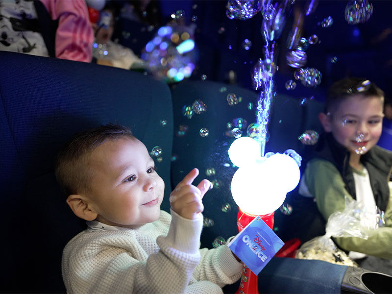 Smiling baby and child watching bubbles and a glowing Mickey Mouse wand at a show or event