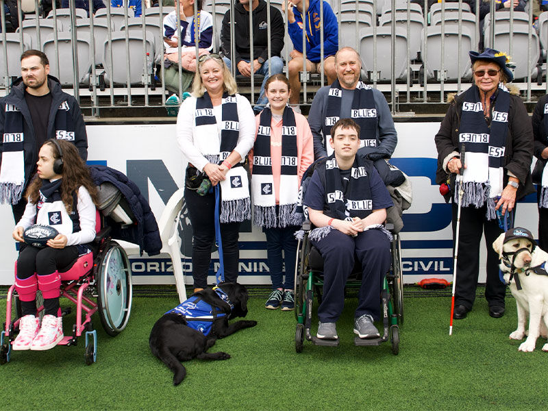 A group of diverse individuals, including people in wheelchairs and with service animals, at a sporting event, all wearing black and white team scarves