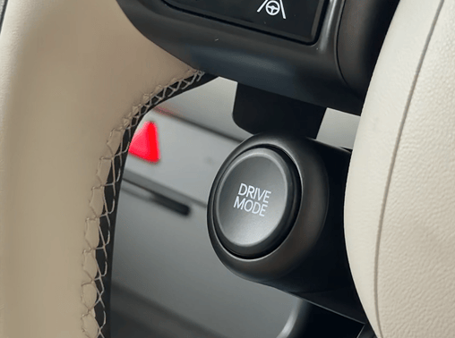 Close-up of the textured, cream-colored leather steering wheel in a Hyundai ELEXIO, highlighting the circular black "Drive Mode" selector button mounted on the lower hub.