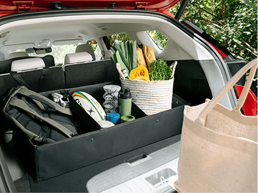 View inside the open trunk of a red Hyundai ELEXIO, showcasing an organized cargo liner tray filled with grocery bags, fresh vegetables, a backpack, and a rugby ball.