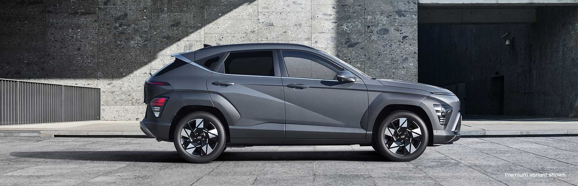 Side profile of the Hyundai KONA set against a modern concrete backdrop, highlighting its sharp design lines and stylish alloy wheels.
