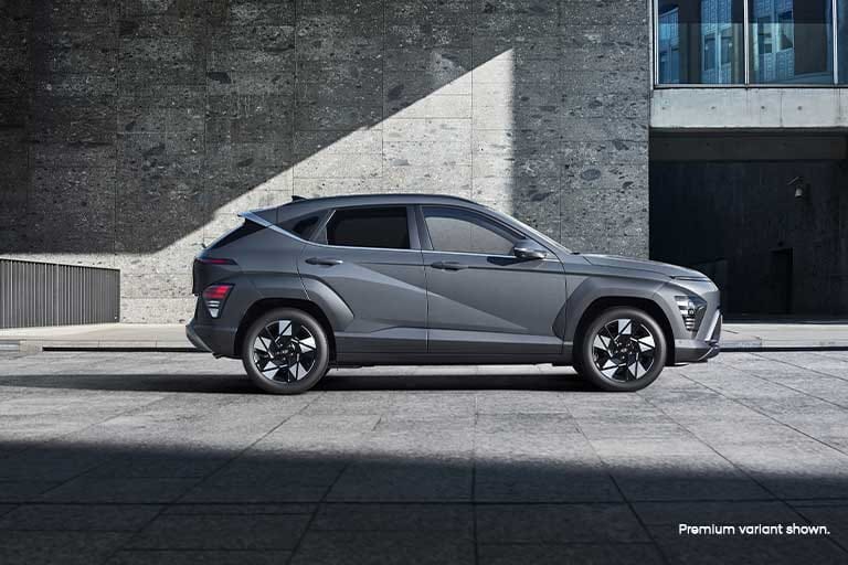 Side profile of the Hyundai KONA set against a modern concrete backdrop, highlighting its sharp design lines and stylish alloy wheels.