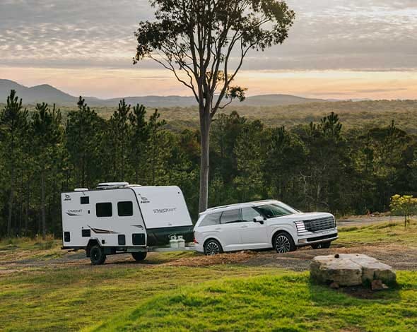 Hyundai PALISADE towing a compact caravan in a scenic outdoor setting, showcasing impressive towing capability, comfort, and versatility for family road trips and camping adventures.