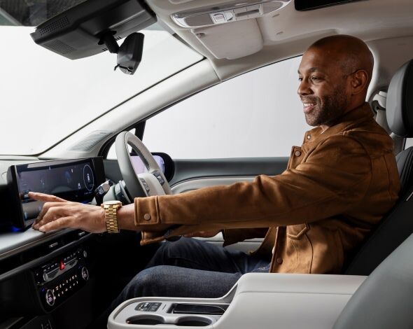 A man seated in the driver's seat of the Hyundai IONIQ 9, smiling as he interacts with the sleek digital touchscreen display, highlighting the vehicle's advanced technology and premium interior design.
