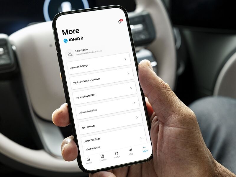 A person holding a smartphone inside the Hyundai IONIQ 9, displaying the vehicle’s connected app interface with options like Vehicle Digital Key, Vehicle & Service Settings, and App Settings, showcasing seamless digital integration and control.