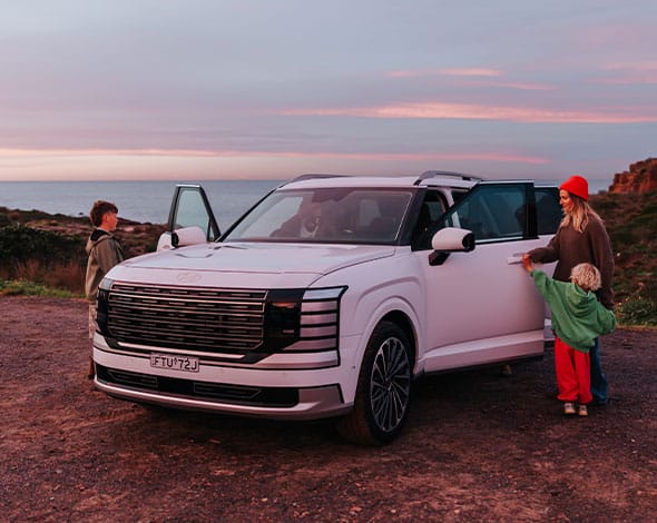 Hyundai PALISADE SUV parked by the coast at sunset with passengers entering and exiting the vehicle, showcasing premium comfort, spaciousness, and family-friendly versatility.