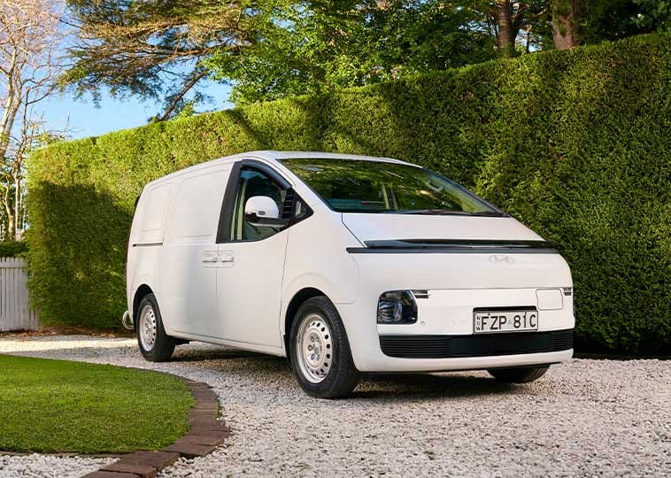 Hyundai STARIA Load EV parked in a landscaped residential driveway, showcasing the all-electric commercial van's modern design, practicality, and everyday versatility.