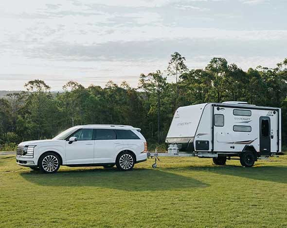 Hyundai PALISADE towing a Jayco Starcraft caravan through a scenic bushland campsite, showcasing strong towing capability, comfort, and versatility for family road trips and outdoor adventures.