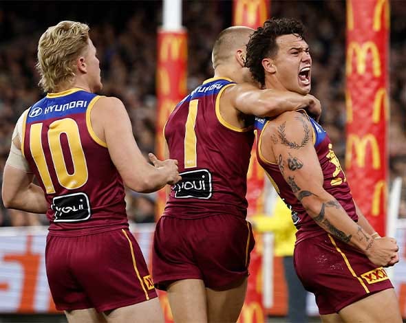 The Brisbane Lions celebrate their AFL Grand Final victory with the trophy, smiling and cheering together on the field after an incredible performance.