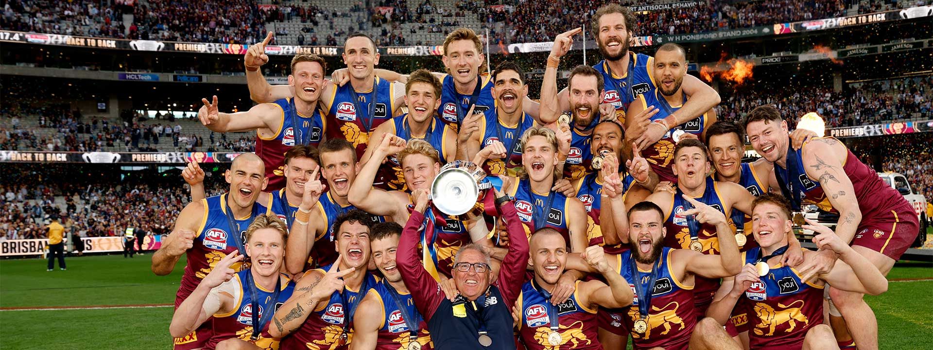 The Brisbane Lions celebrate their AFL Grand Final victory with the trophy, smiling and cheering together on the field after an incredible performance.