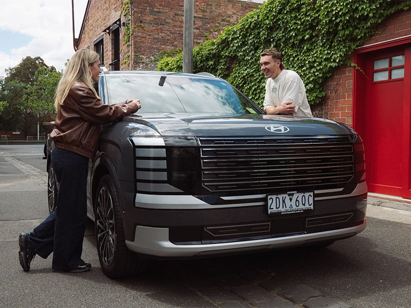 A Hyundai IONIQ 9 parked on a leafy urban street in Victoria, Australia, framed by ivy-covered brick and casual conversation, highlighting modern design, lifestyle appeal, and local presence.