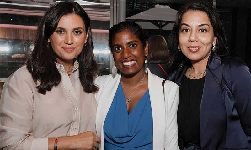 Three professional women smiling, networking at an event