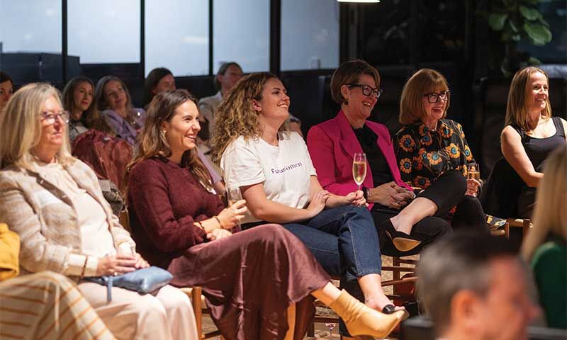 Women smiling and engaging at a professional event, with one holding a glass of champagne