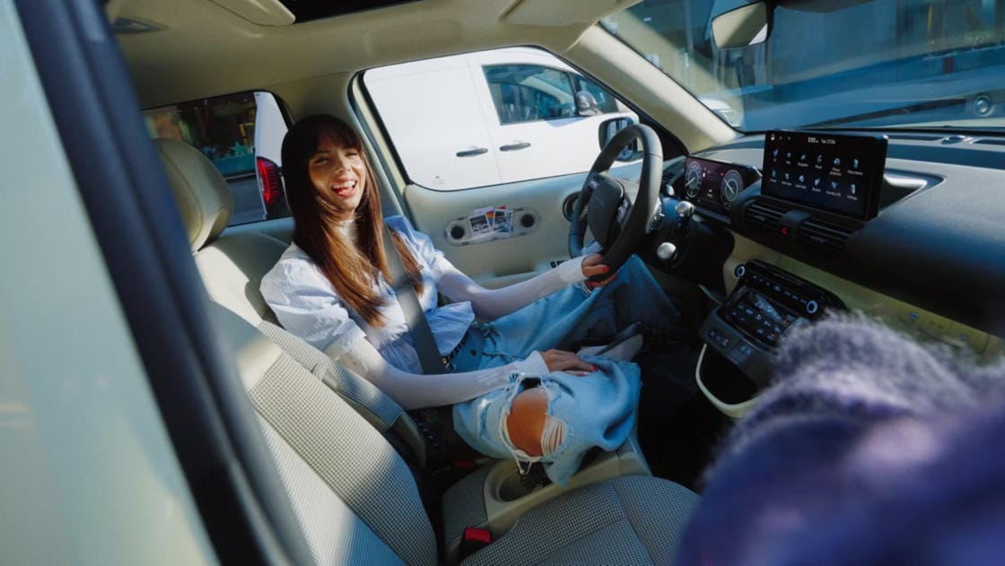 Una mujer se relaja en el interior del nuevo coche eléctrico compacto Hyundai INSTER, mostrando su interior espacioso y moderno.