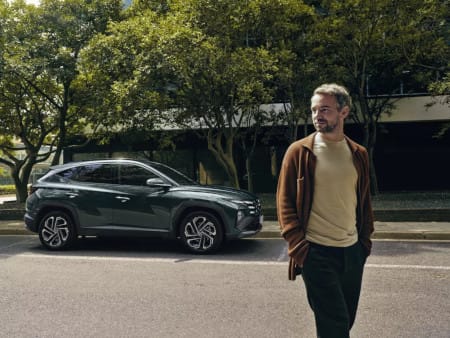 El Hyundai TUCSON aparcado en una calle arbolada con un hombre alejándose de él.