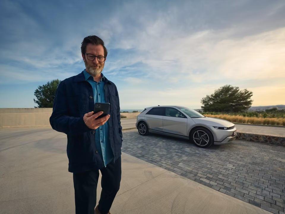 Hyundai IONIQ 5 en el fondo. Una persona está revisando la aplicación myHyundai.