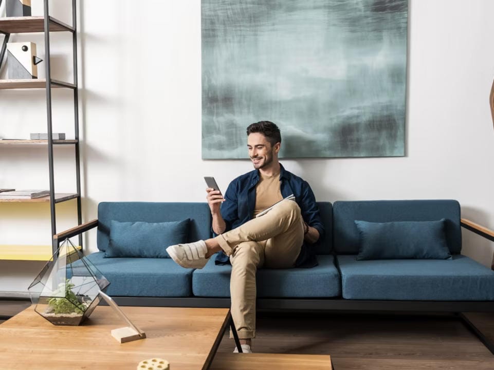 Hombre en el sofá de su sala de estar sentado con las piernas cruzadas. Está usando su aplicación myHyundai.