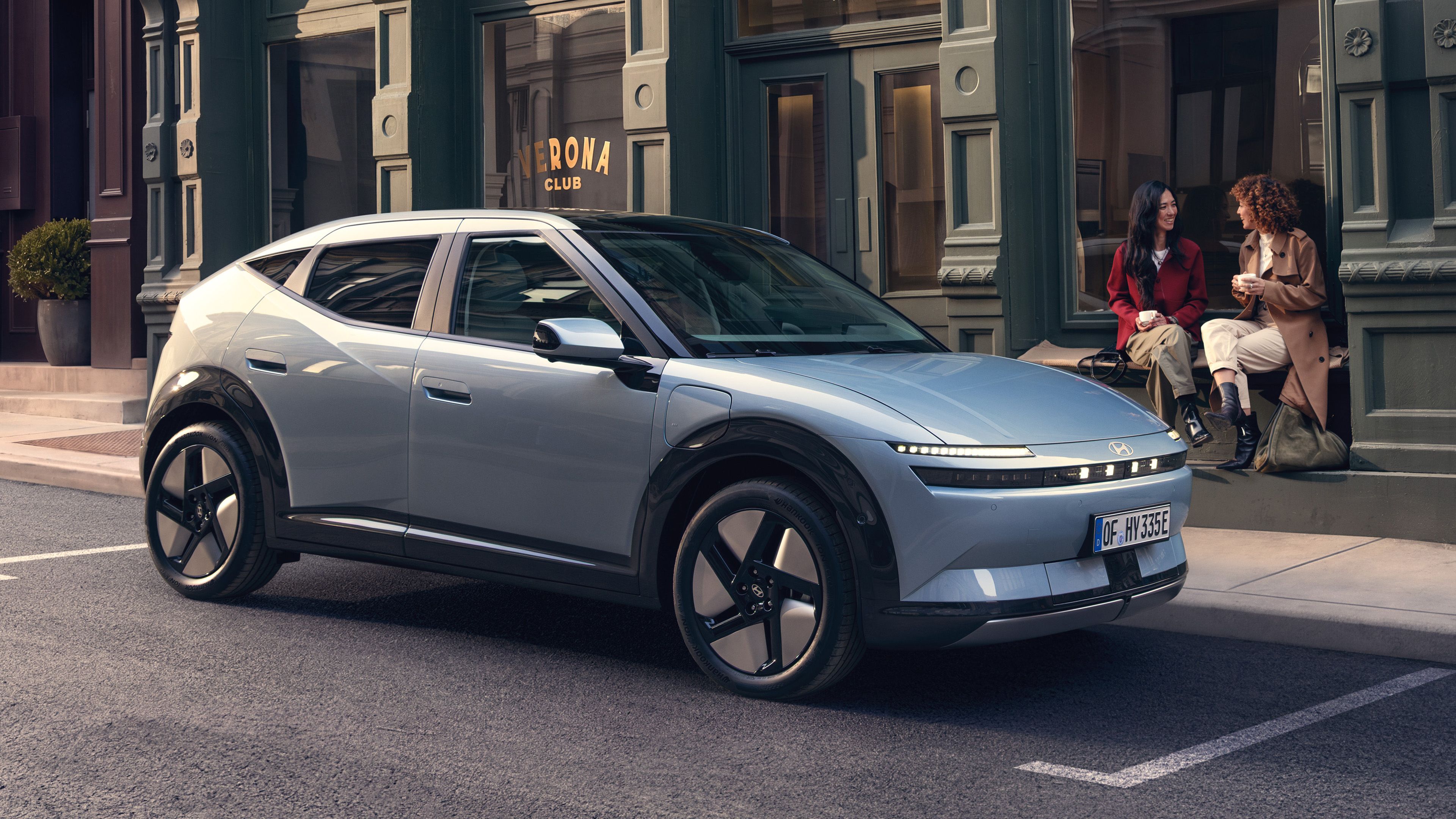 Hyundai IONIQ 3 EV parked on a city street with two woman sitting on a stoop next to it.
