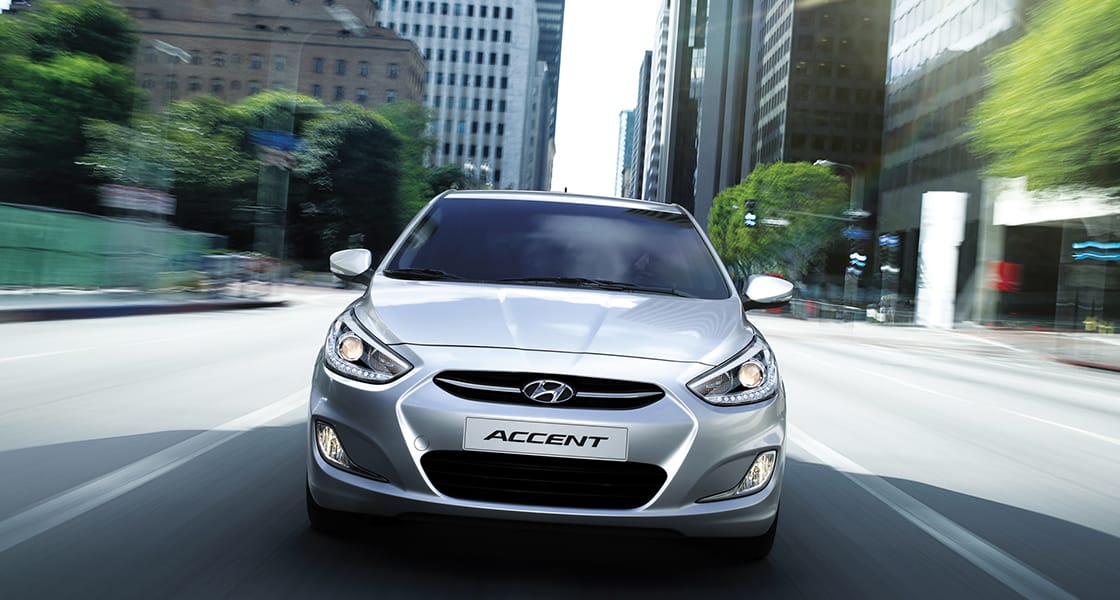 Front view of silver Accent5DR driving fast through the buildings in the city