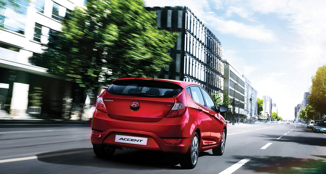 Rear view of red Accent5DR driving fast through the building in the city